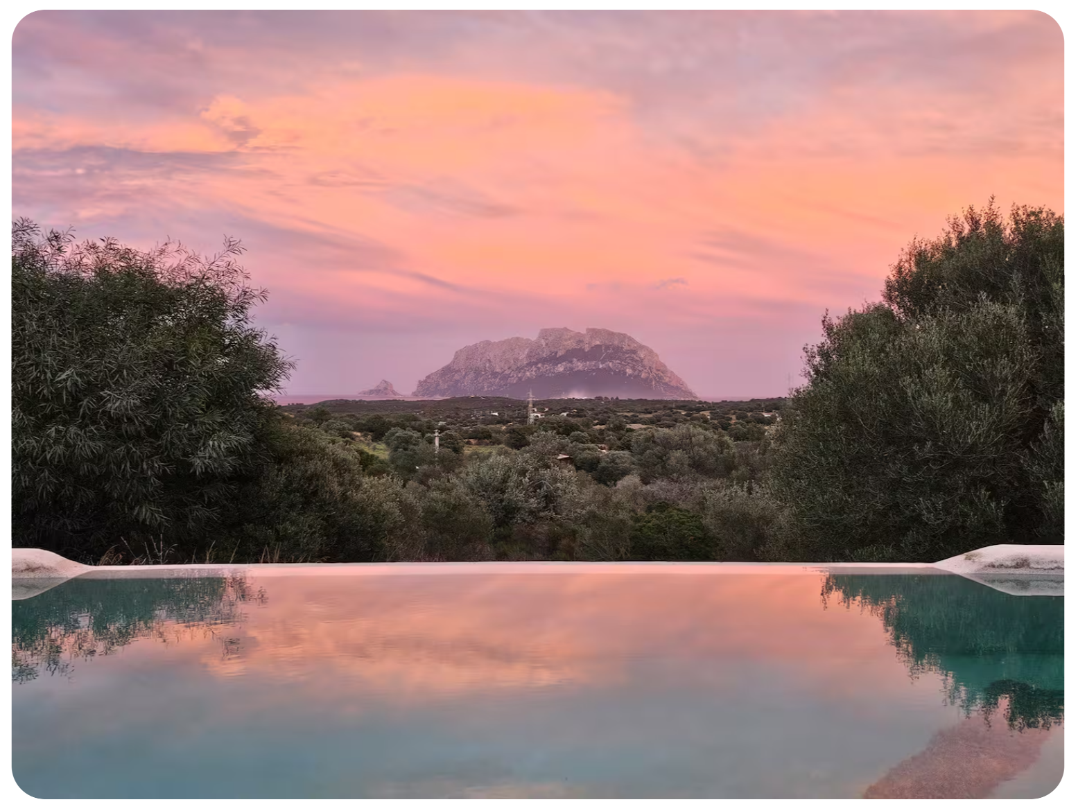 Infinity pool at dusk reflecting a pink Sardinian sky with Tavolara island on the horizon